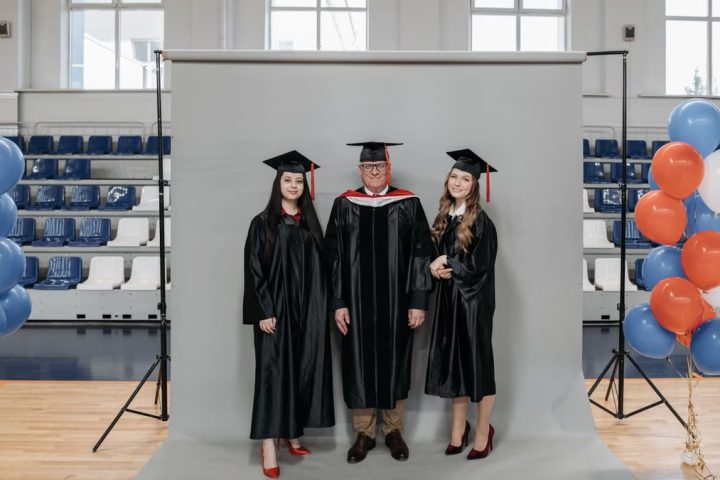 Group graduation portrait with caps and gowns in gymnasium setting.